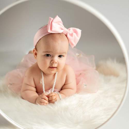 baby in soft pink attire and pearl necklace, lying on plush faux fur