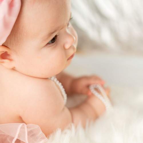 Portrait of an adorable baby girl with a pink headband and pearl necklace on a fluffy rug background
