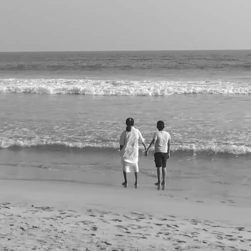 A serene, lighter-toned monochrome image of an adult and a child standing in the shallow surf.