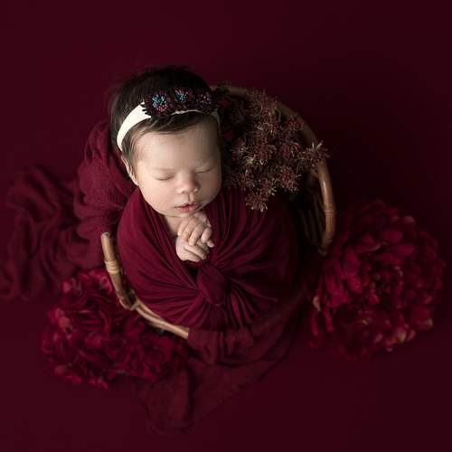 Newborn girl surrounded by red flowers