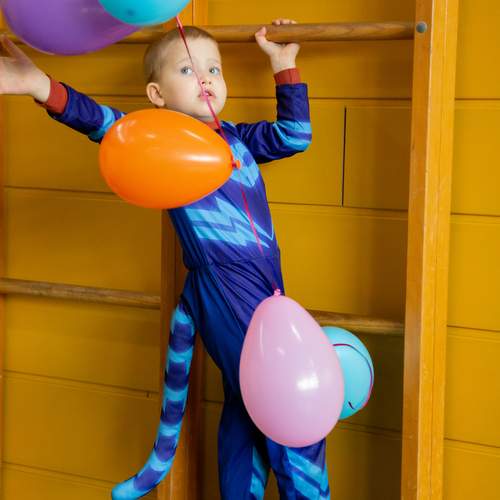A vertical medium portrait photograph focusing on a young child wearing a blue superhero carnival costume holding colorful balloons next to wooden wall bars