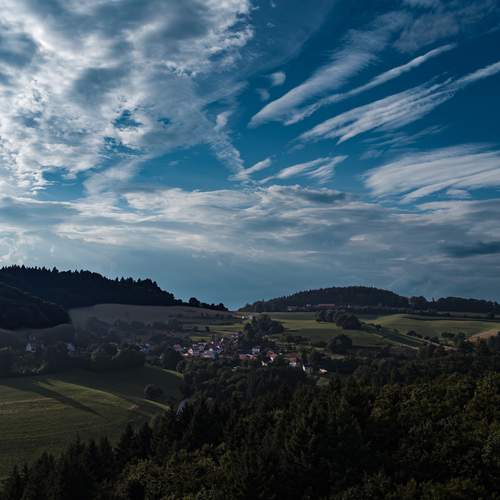 A magnificent high angle aerial drone photograph showing a peaceful village surrounded by dense picea abies spruce forests under a dramatic cloudy sky