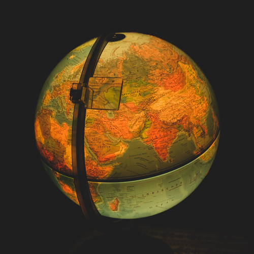A beautiful detailed close up conceptual photograph showing a glowing vintage illuminated terrestrial globe map with eurasia continent details against a dark black background during a sunny day