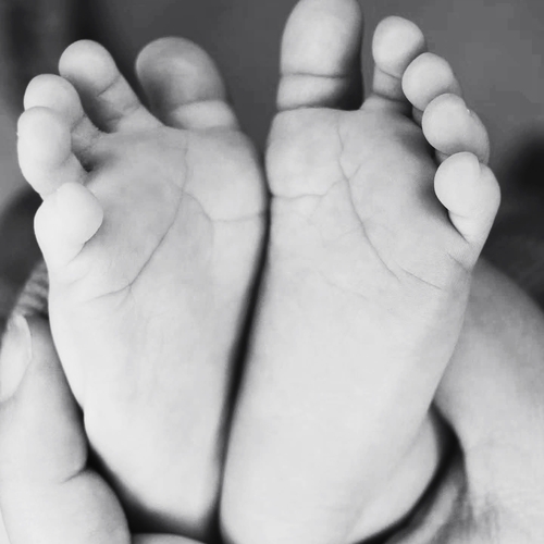 Black and white portrait photograph of a parents hands gently cradling tiny newborn baby feet showing sole details and small toes