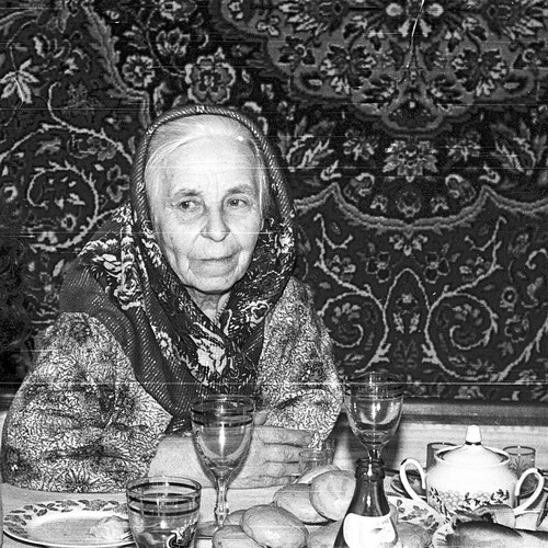 Пожилая женщина, сидящая за праздничным столом в доме