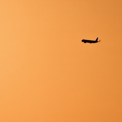 Minimal Airplane Against Solid Orange Sky