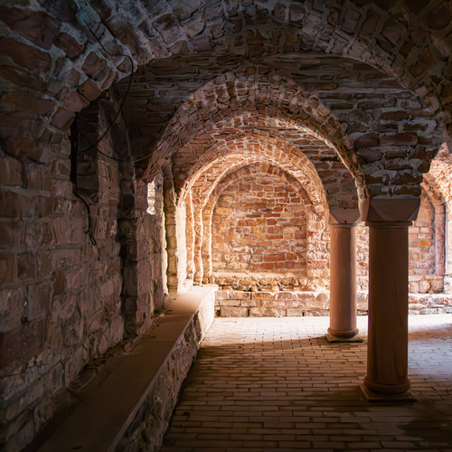 A detailed wide interior photo showing historic medieval stone crypt with arched brick vaults sturdy round columns and brick floor