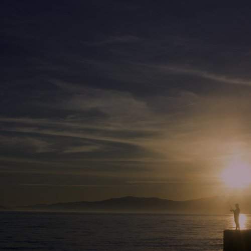 Little boy is fishing at sunset